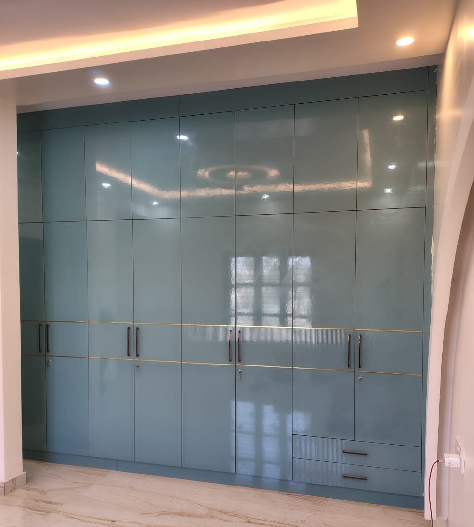 Full-height wardrobe wall in high-gloss teal lacquer, by Padmodya Interiors